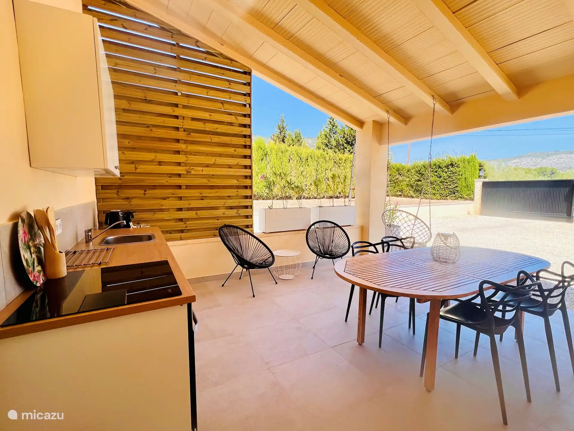 Su terraza privada en el apartamento. Con cocina exterior totalmente equipada, con placa de inducción y horno. Mesa de comedor con 4 sillas y 2 sillas bajas. Con impresionantes vistas sobre la Sierra Mariola.
