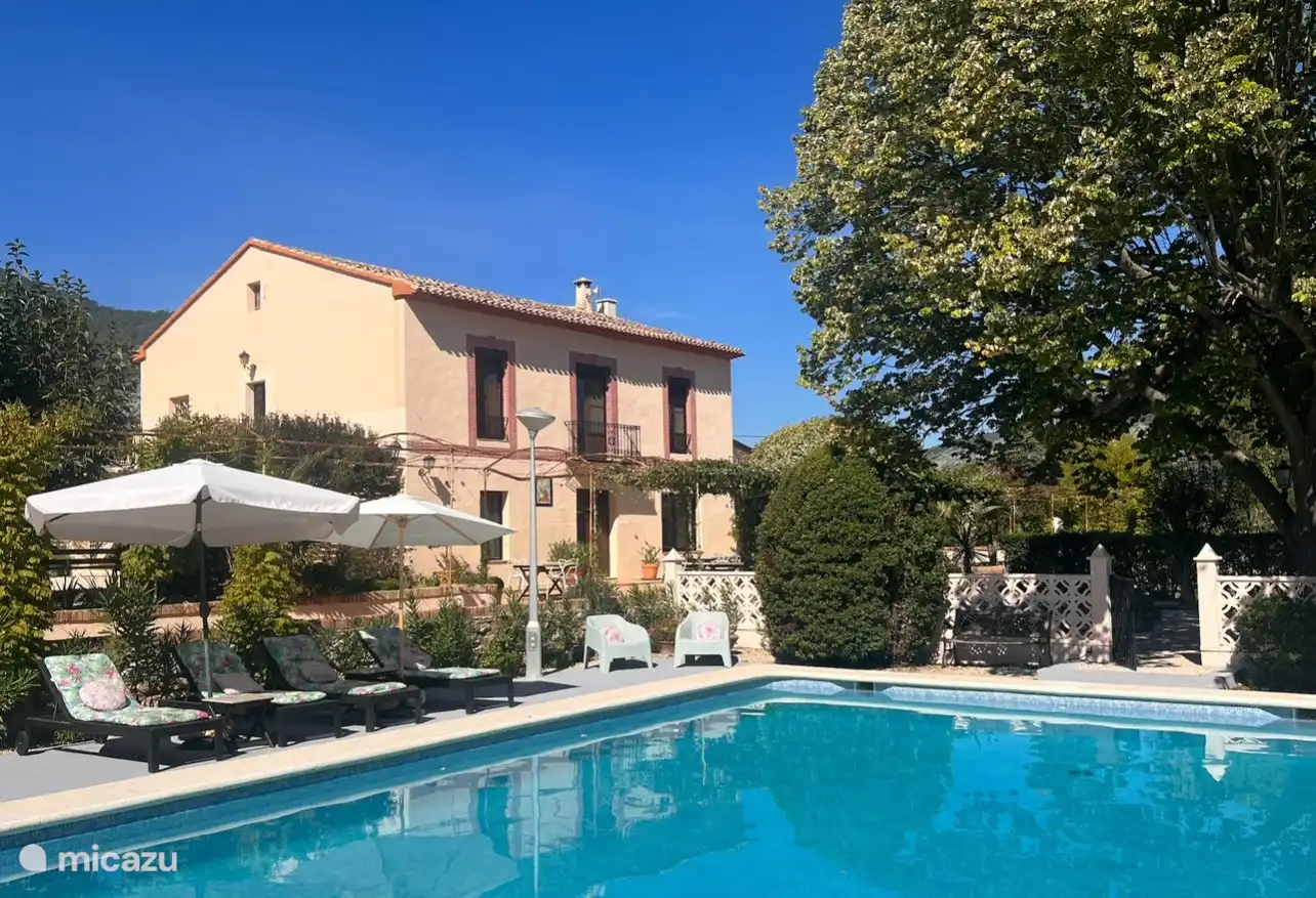 La casa principal vista desde la piscina. Su apartamento con terraza privada se encuentra en la parte trasera de la casa principal. El gran tilo proporciona sombra natural en el jardín. 
