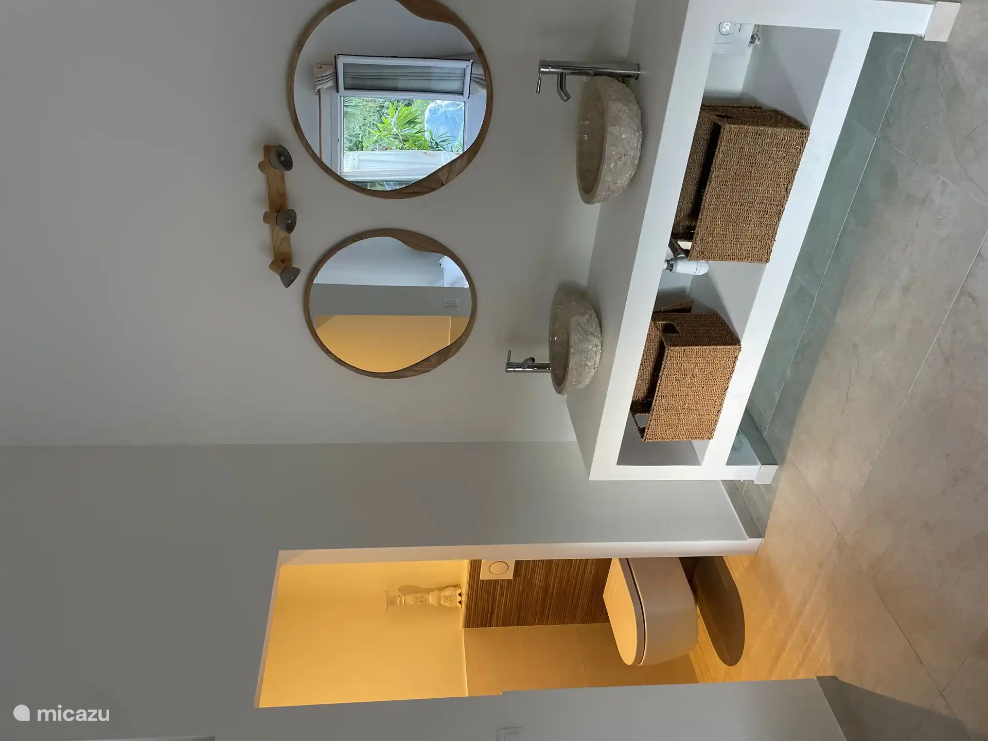 De ruime masterbedroom combineert strak design met natuurlijke materialen met een ensuit badkamer met natuurstenen waskommen en inloop douche.