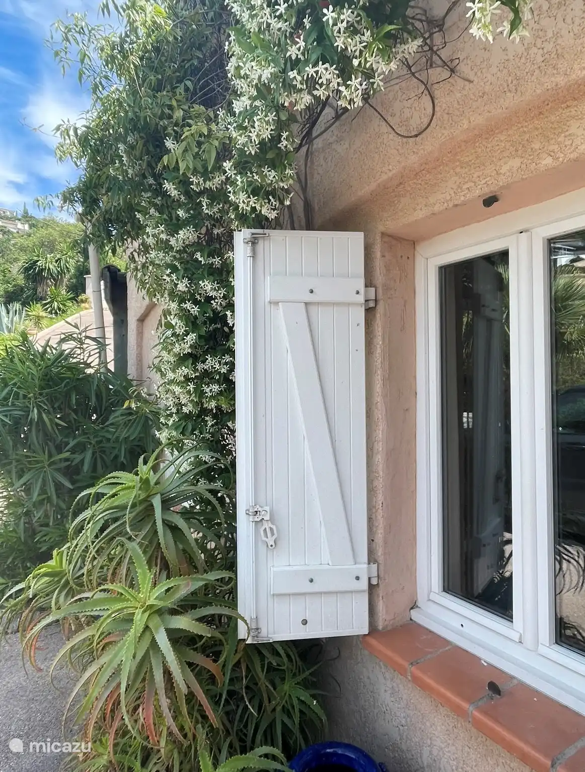 Direct grenzend aan de slaapkamer biedt dit openslaande raam uitzicht op een weelderige tuin vol mediterrane planten. De bloeiende Jasmijn verspreid een heerlijke geur.