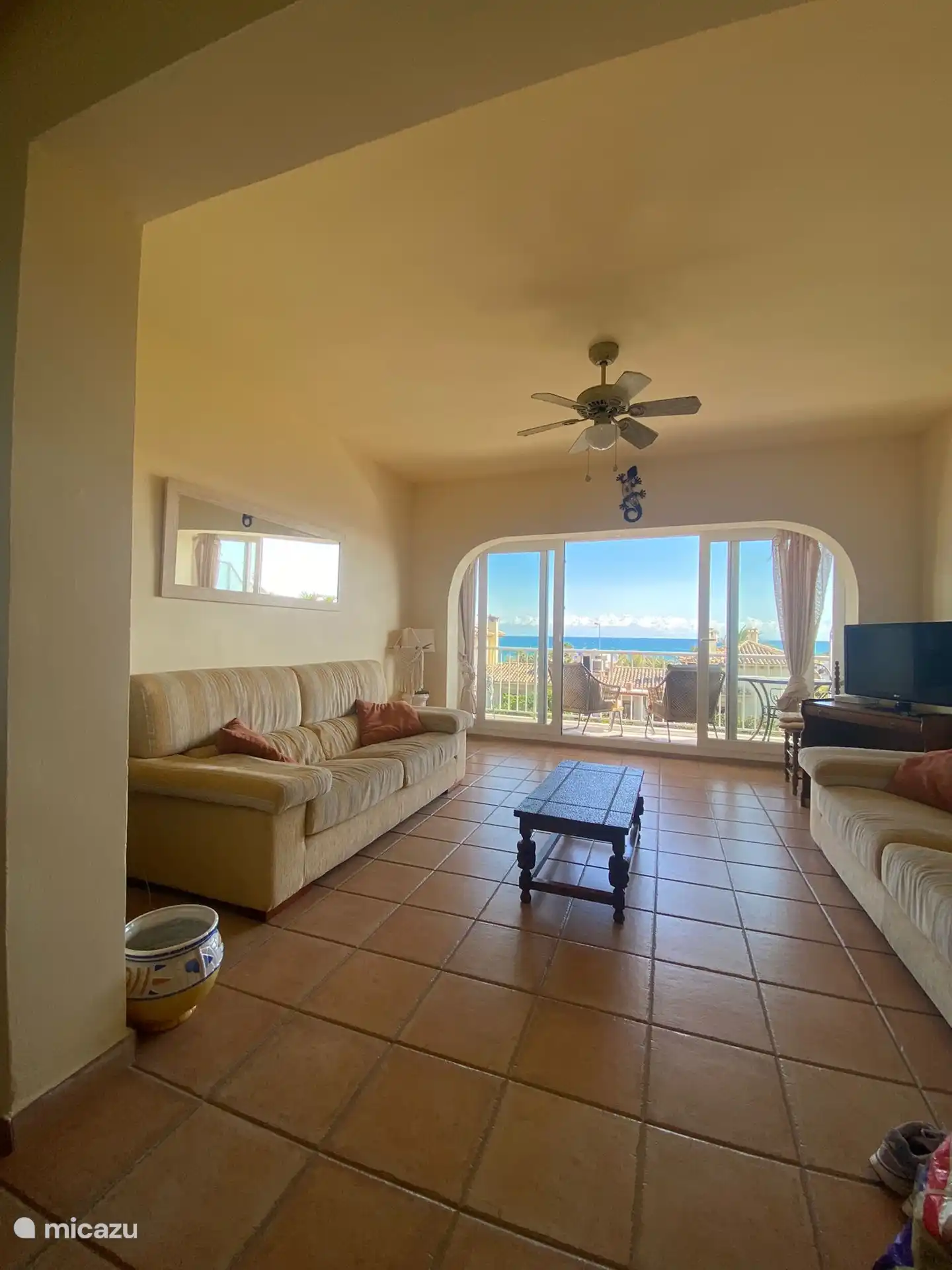 The living room has a ceiling fan, a flat screen tv with lots of TV channels.