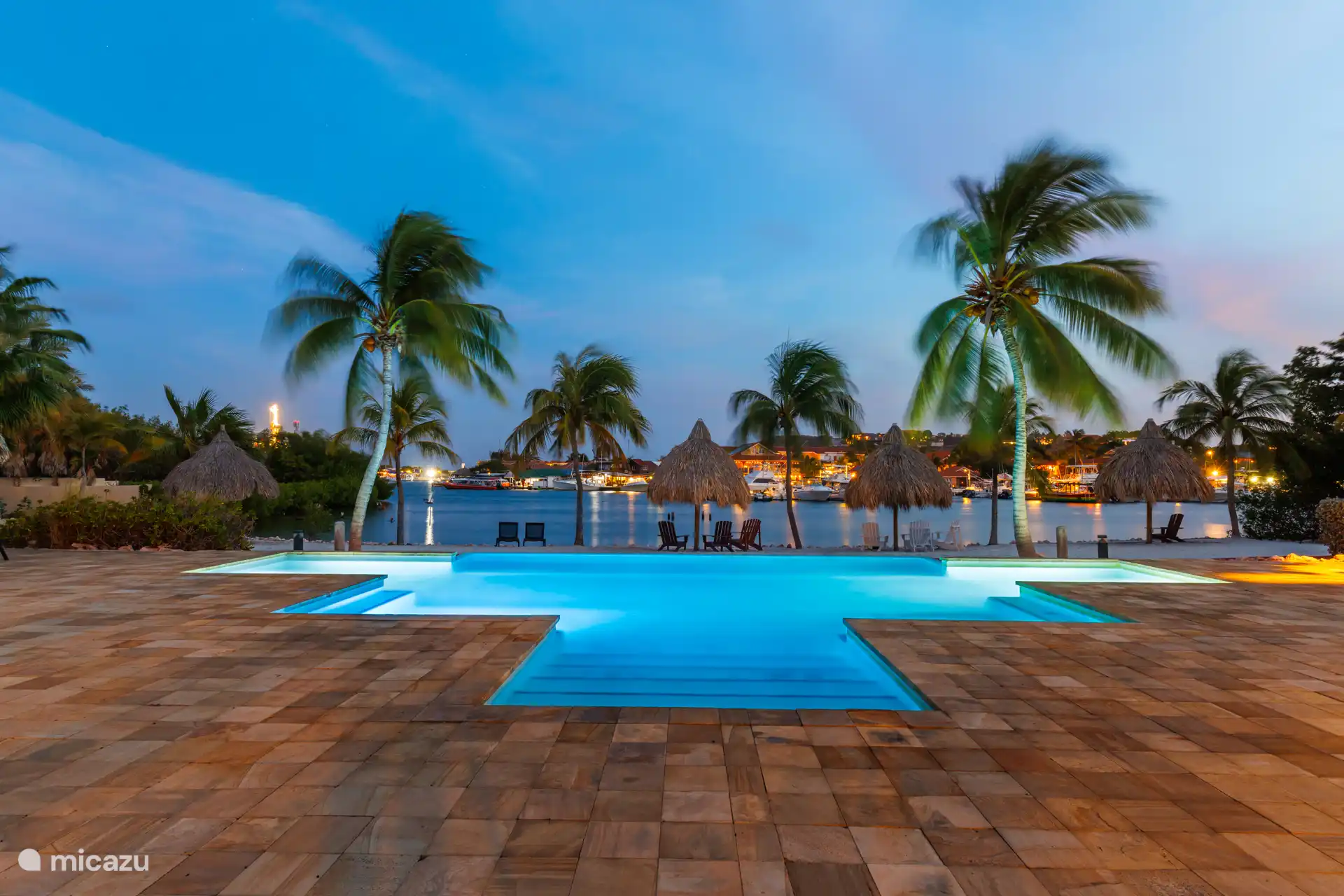 Piscina infinita justo en la playa privada con tumbonas y sillas.