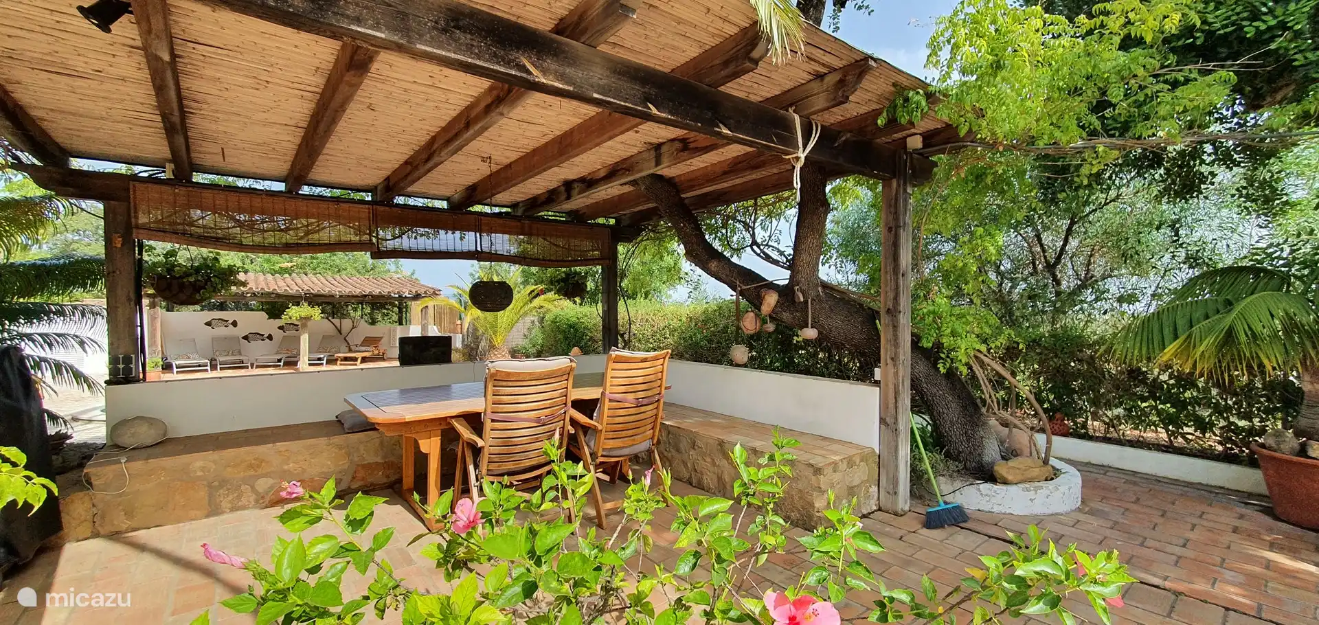 Überdachte Terrasse mit Esstisch, Stühlen, eingebauten Bänken und dem Gasgrill.