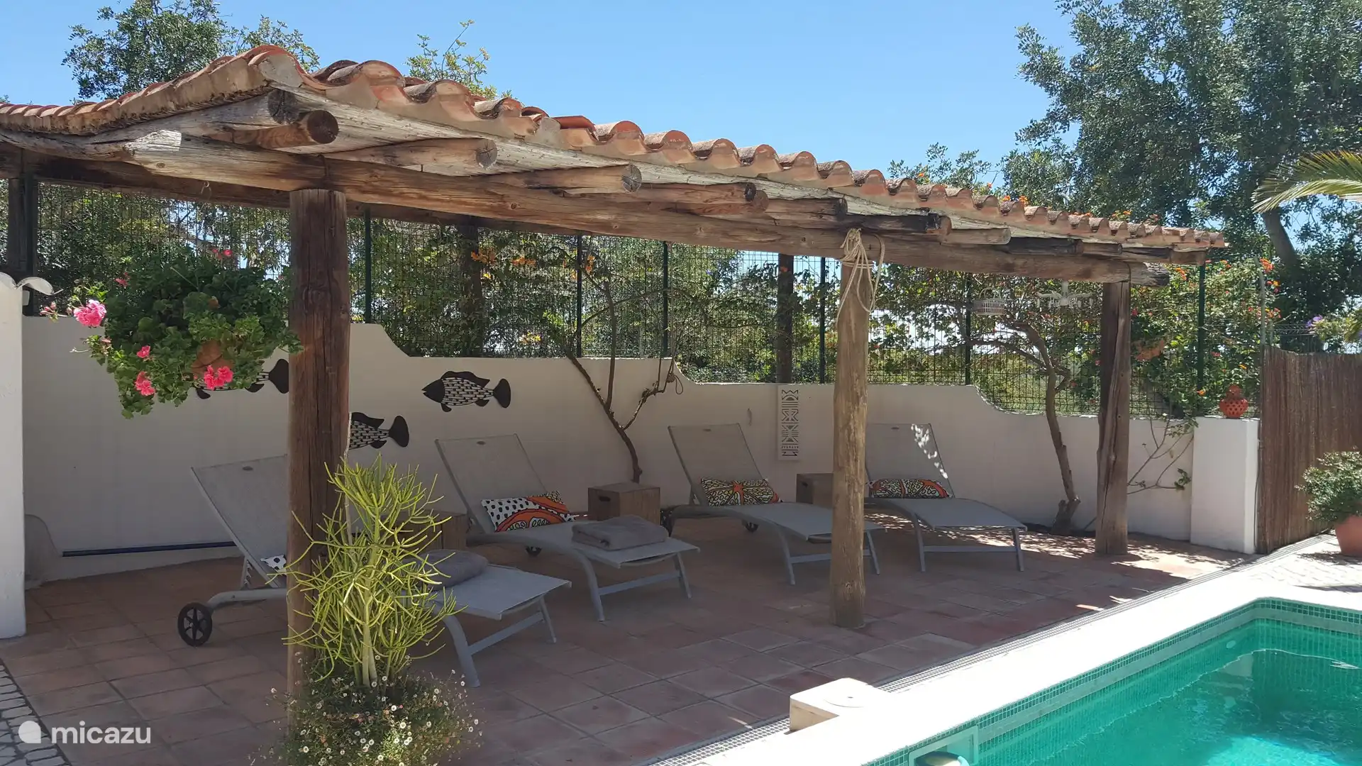 Überdachte Terrasse am Pool mit Sonnenliegen.