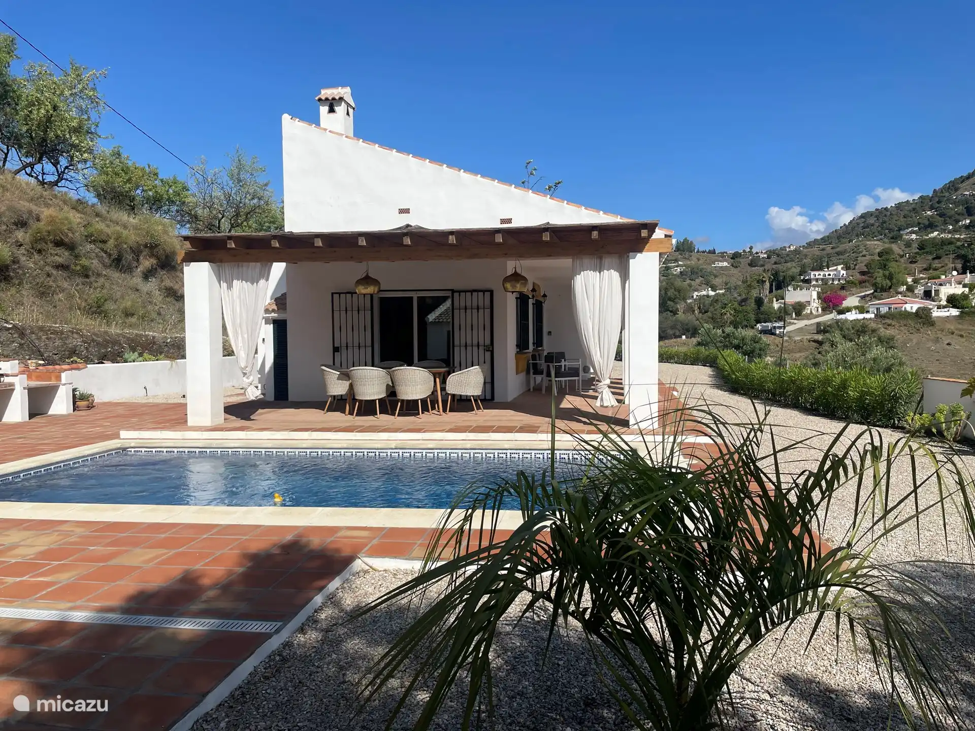 Grand espace extérieur avec plusieurs tables, chaises, transats et coins salon. Belle vue sur les montagnes, entourée de bois, de terres agricoles et de jardins.