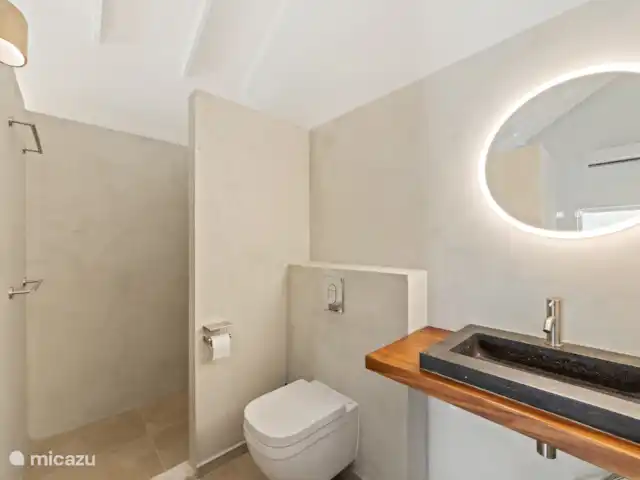 Villa Blenchi Curaçao Zwembad & Tuin huren in Curaçao, Curacao-Midden, Willemstad - vakantiehuis Lichte badkamer met regendouche, natuurstenen wastafel en modern hangtoilet. Afgewerkt met warme materialen en indirecte verlichting voor een rustgevende sfeer