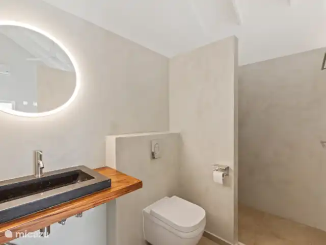 Villa Blenchi Curaçao Zwembad & Tuin huren in Curaçao, Curacao-Midden, Willemstad - vakantiehuis Lichte badkamer met regendouche, natuurstenen wastafel en modern hangtoilet. Afgewerkt met warme materialen en indirecte verlichting voor een rustgevende sfeer