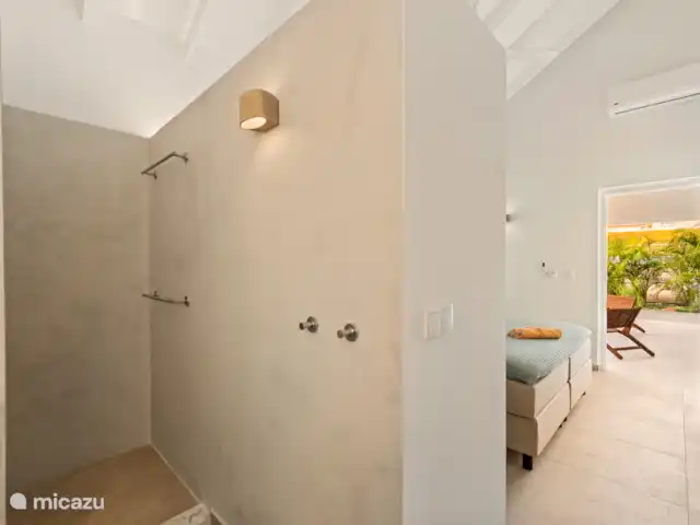 Villa Blenchi Curaçao Zwembad & Tuin huren in Curaçao, Curacao-Midden, Willemstad - vakantiehuis Lichte badkamer met regendouche, natuurstenen wastafel en modern hangtoilet. Afgewerkt met warme materialen en indirecte verlichting voor een rustgevende sfeer