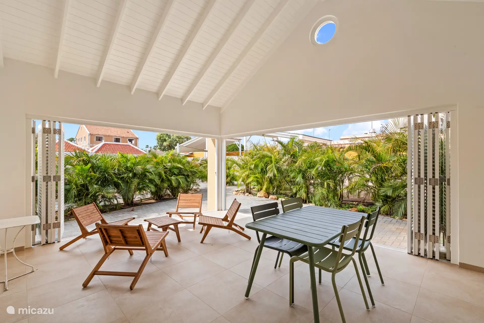 Interior space of Villa Awa with sitting area and dining table, adjacent to the terrace overlooking tropical greenery. Large shutter doors provide light, air and privacy