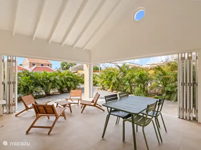 Resort privé Curaçao pour les groupes | Curaçao, Curaçao-Centre, Willemstad - villa Espace intérieur de la Villa Awa avec coin salon et table à manger, adjacent à la terrasse donnant sur la verdure tropicale. De grandes portes à volets assurent la lumière, l’air et l’intimité