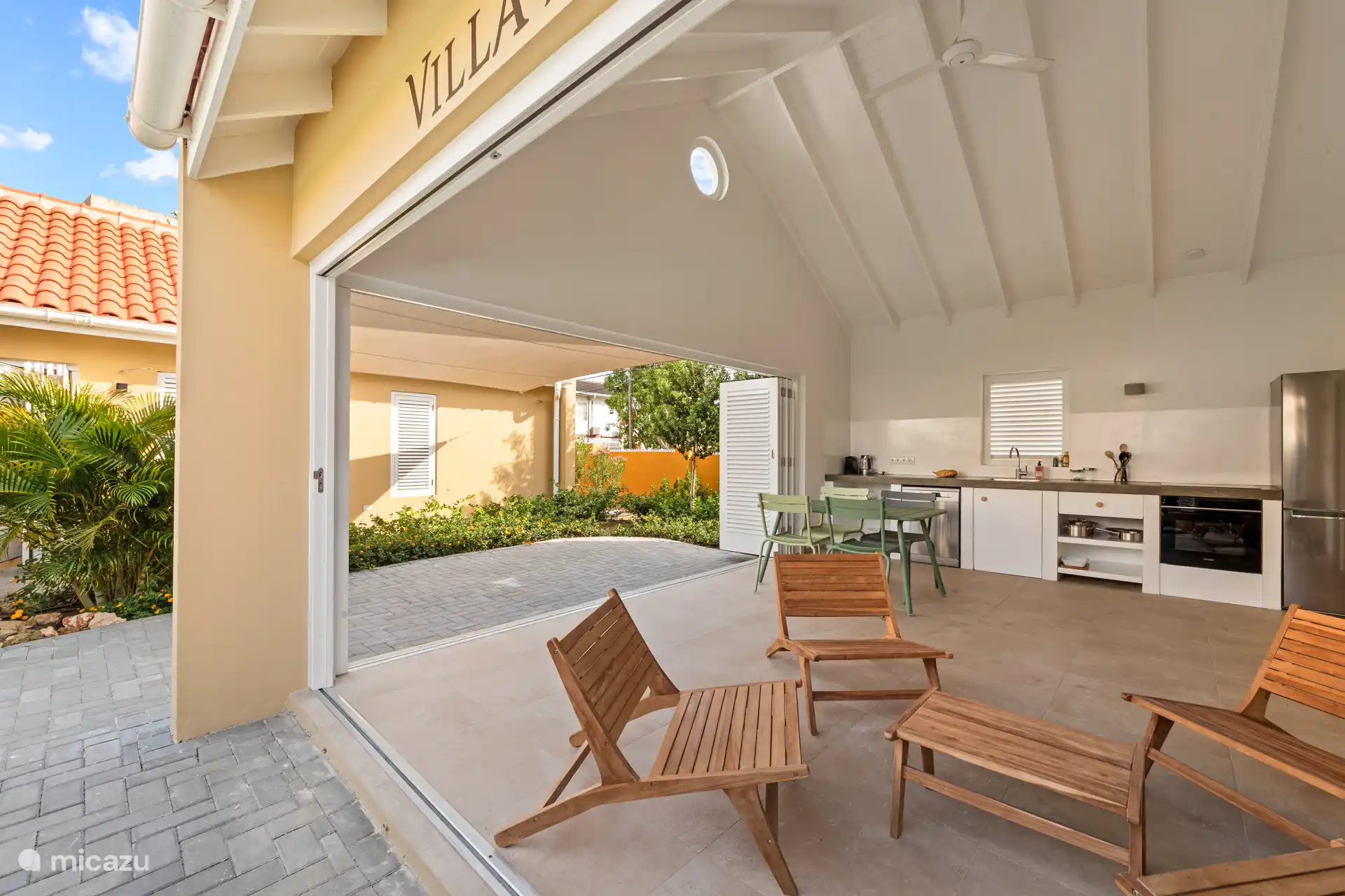 Villa Awa with open kitchen, dining table and sitting area under high ceiling with ceiling fan. Large sliding doors connect the interior with the tropical greenery and the spacious terrace