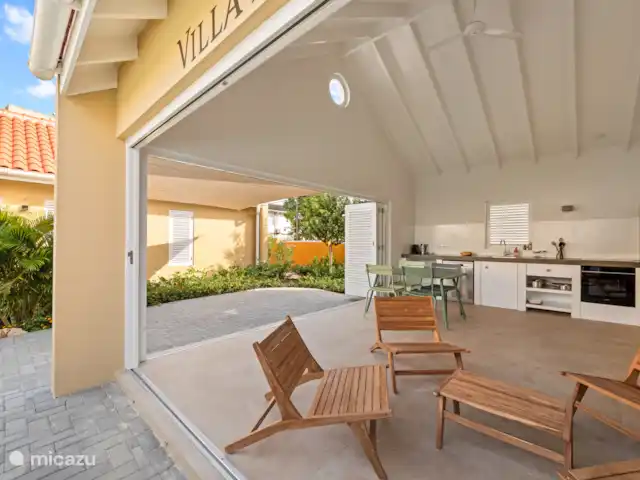 Resort privé Curaçao pour les groupes | Curaçao, Curaçao-Centre, Willemstad - villa Villa Awa avec cuisine ouverte, table à manger et coin salon sous haut plafond avec ventilateur de plafond. De grandes portes coulissantes relient l’intérieur à la verdure tropicale et à la terrasse spacieuse