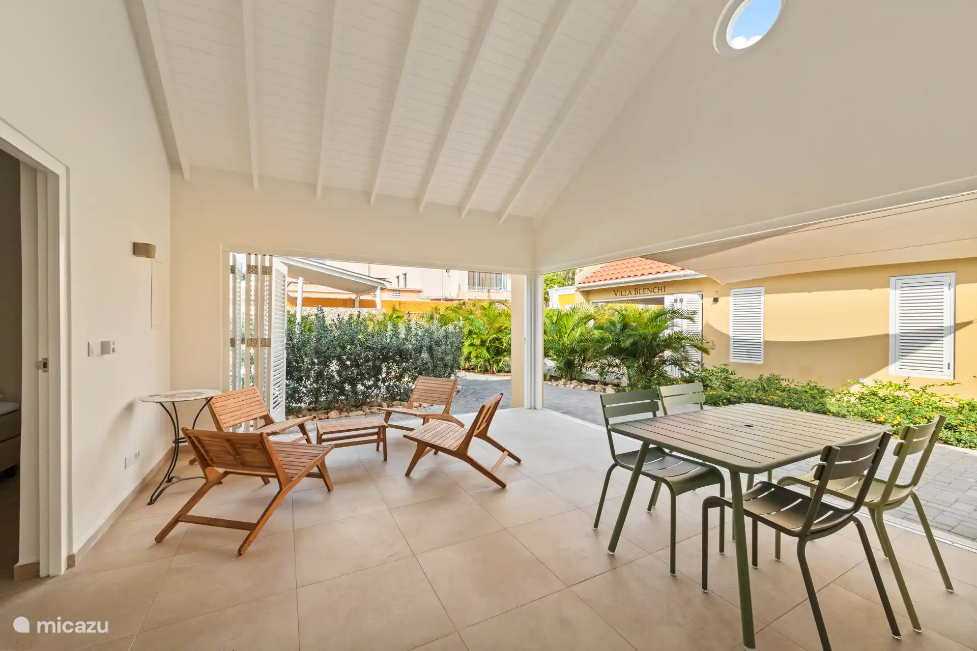 Indoor space of Villa Awa with sitting area and dining table, adjacent to the terrace overlooking Villa Blenchi and tropical greenery. Large shutter doors provide light, air and privacy