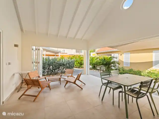 Resort privé Curaçao pour les groupes | Curaçao, Curaçao-Centre, Willemstad - villa Espace intérieur de la Villa Awa avec coin salon et table à manger, adjacent à la terrasse donnant sur la Villa Blenchi et la verdure tropicale. De grandes portes à volets assurent la lumière, l’air et l’intimité