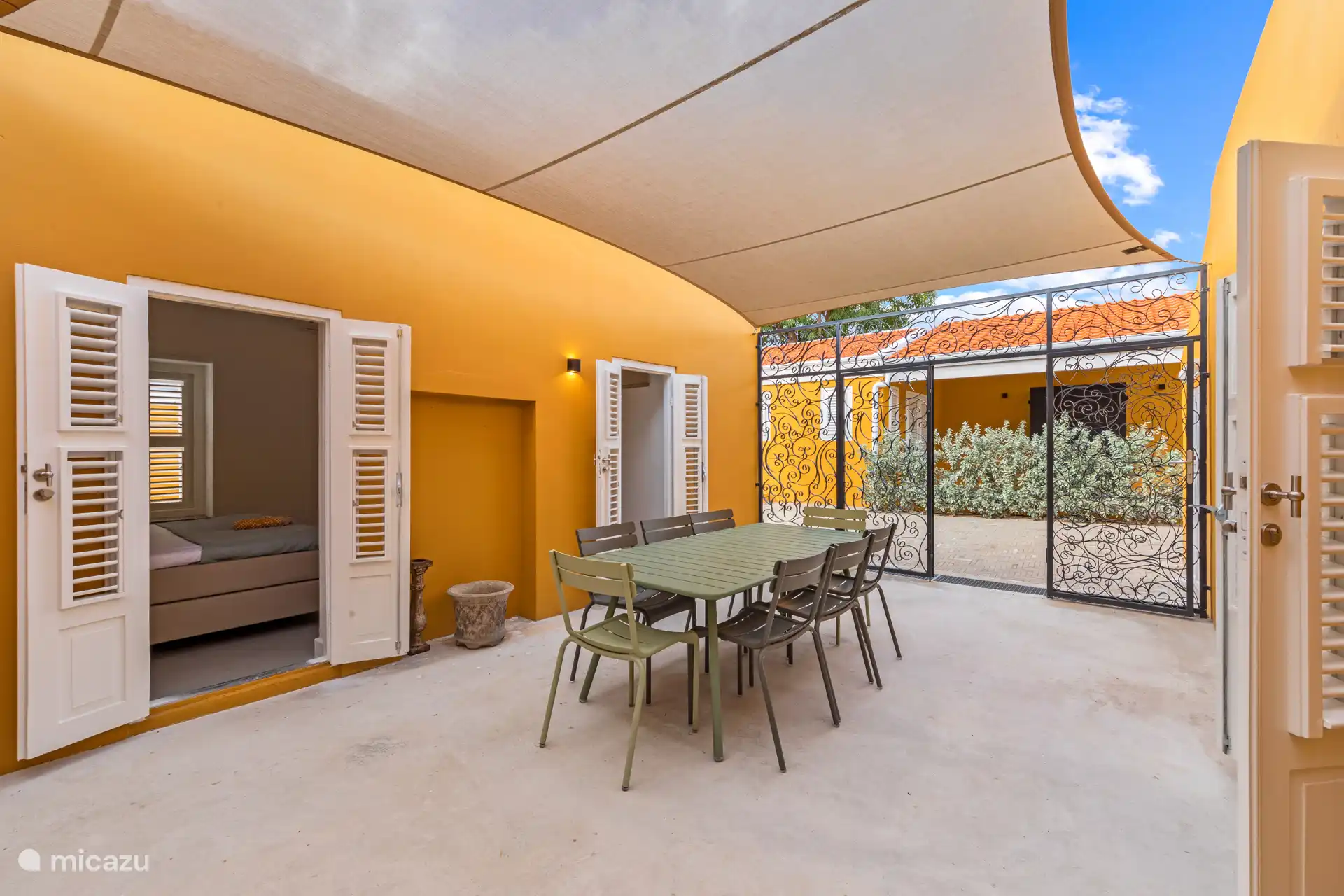 Attractive courtyard with elegant wrought-iron entrance gate, sun canopy and spacious dining table – an intimate place to enjoy the outdoors