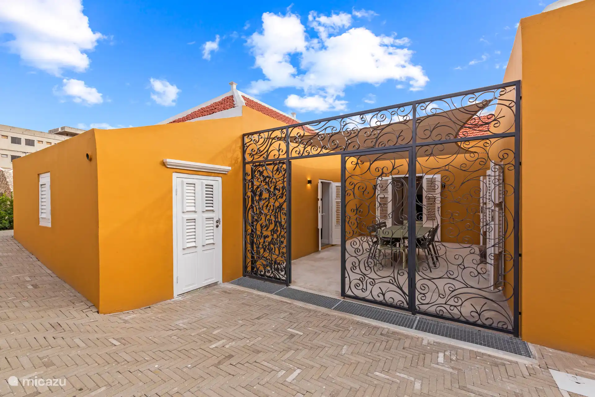 Attractive courtyard with elegant wrought-iron entrance gate, sun canopy and spacious dining table – an intimate place to enjoy the outdoors