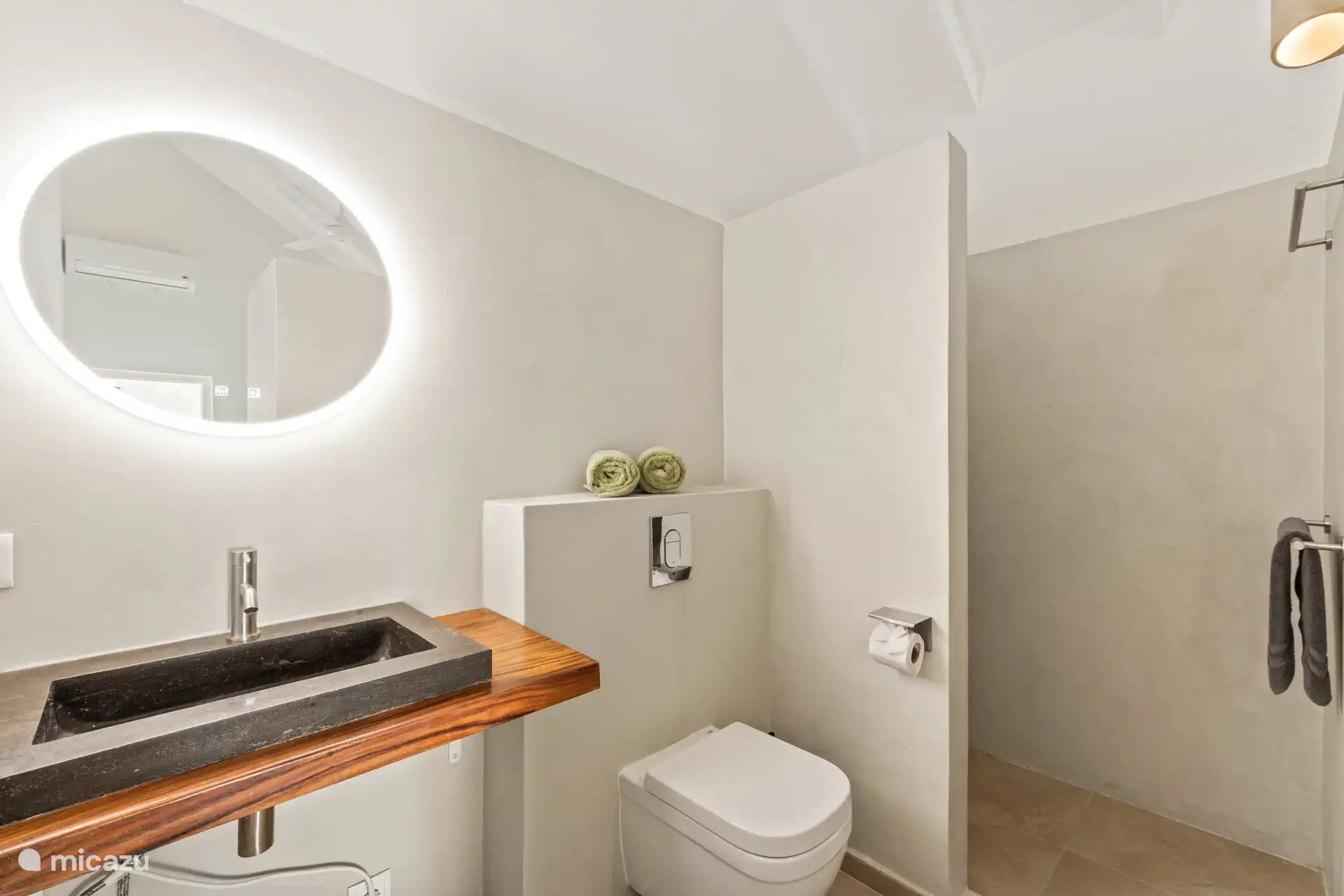 Bright bathroom with rain shower, natural stone sink and modern hanging toilet. Finished with warm materials and indirect lighting for a calming atmosphere