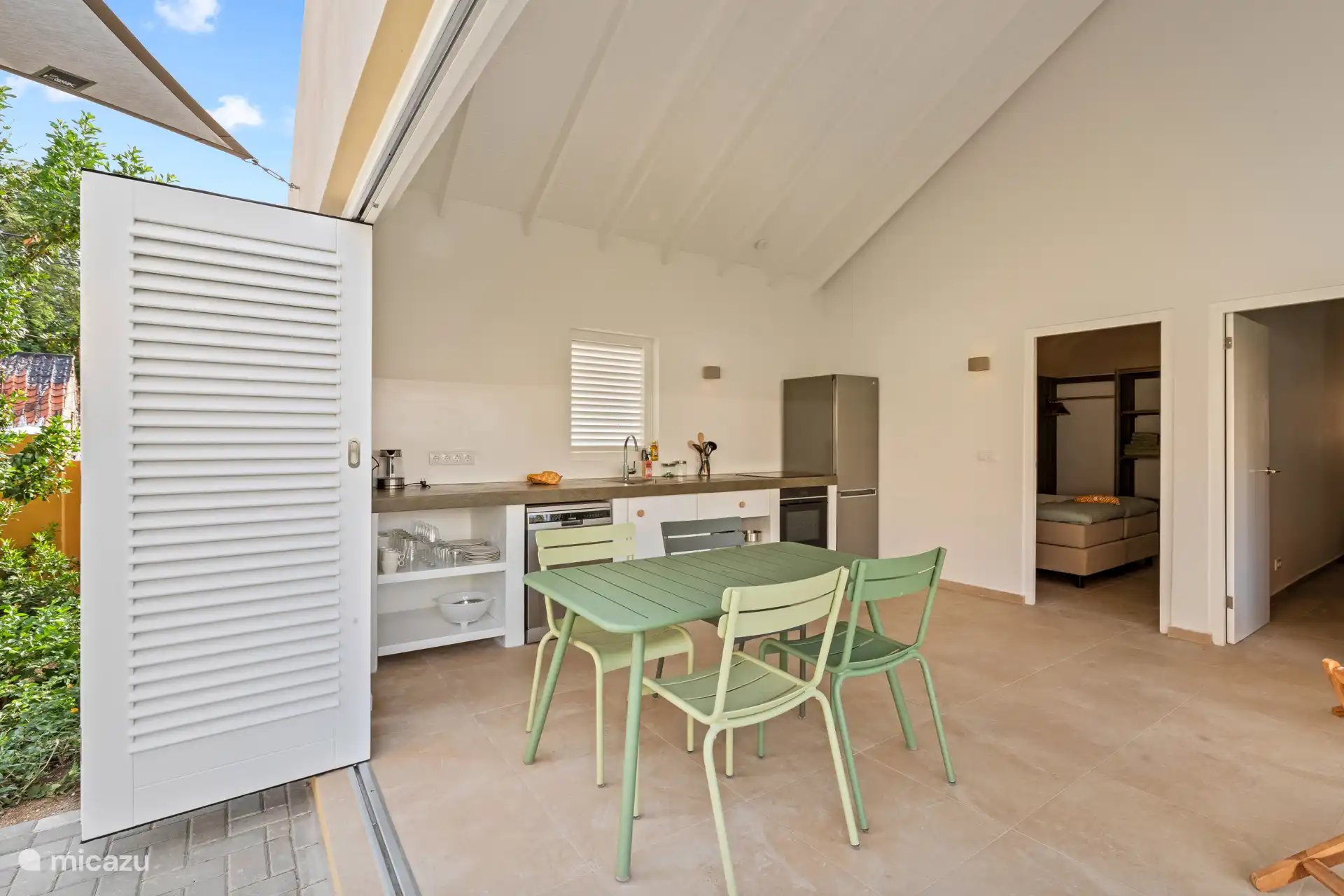 Indoor space of Villa Awa with sitting area and dining table, adjacent to the terrace overlooking Villa Blenchi and tropical greenery. Large shutter doors provide light, air and privacy