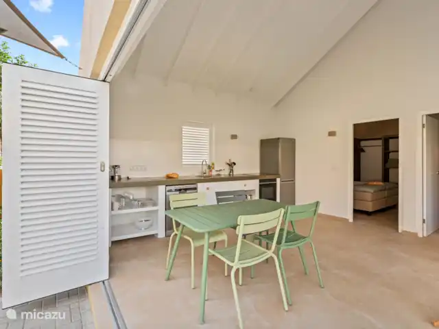 Resort privé Curaçao pour les groupes | Curaçao, Curaçao-Centre, Willemstad - villa Espace intérieur de la Villa Awa avec coin salon et table à manger, adjacent à la terrasse donnant sur la Villa Blenchi et la verdure tropicale. De grandes portes à volets assurent la lumière, l’air et l’intimité