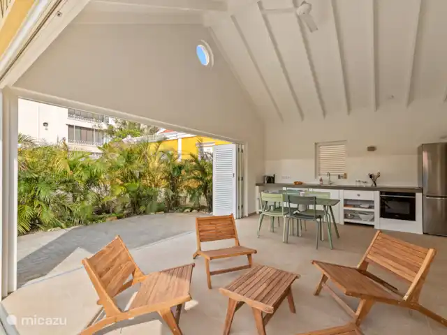 Resort privé Curaçao pour les groupes | Curaçao, Curaçao-Centre, Willemstad - villa Villa Blenchi avec cuisine ouverte, table à manger et coin salon sous un haut plafond avec ventilateur de plafond. De grandes portes coulissantes relient l’intérieur à la verdure tropicale et à la terrasse spacieuse