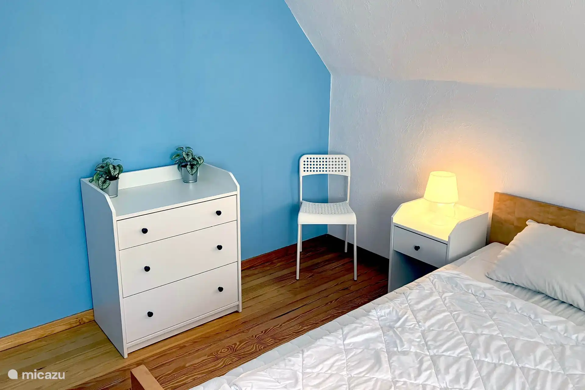 Schlafzimmer im ersten Stock mit Doppelbett und Nachttischen für Erwachsene. Ebenfalls vorhanden: kleiner Kleiderschrank, kleine Kommode mit Spiegel, ein Kleiderständer und ein Stuhl. 