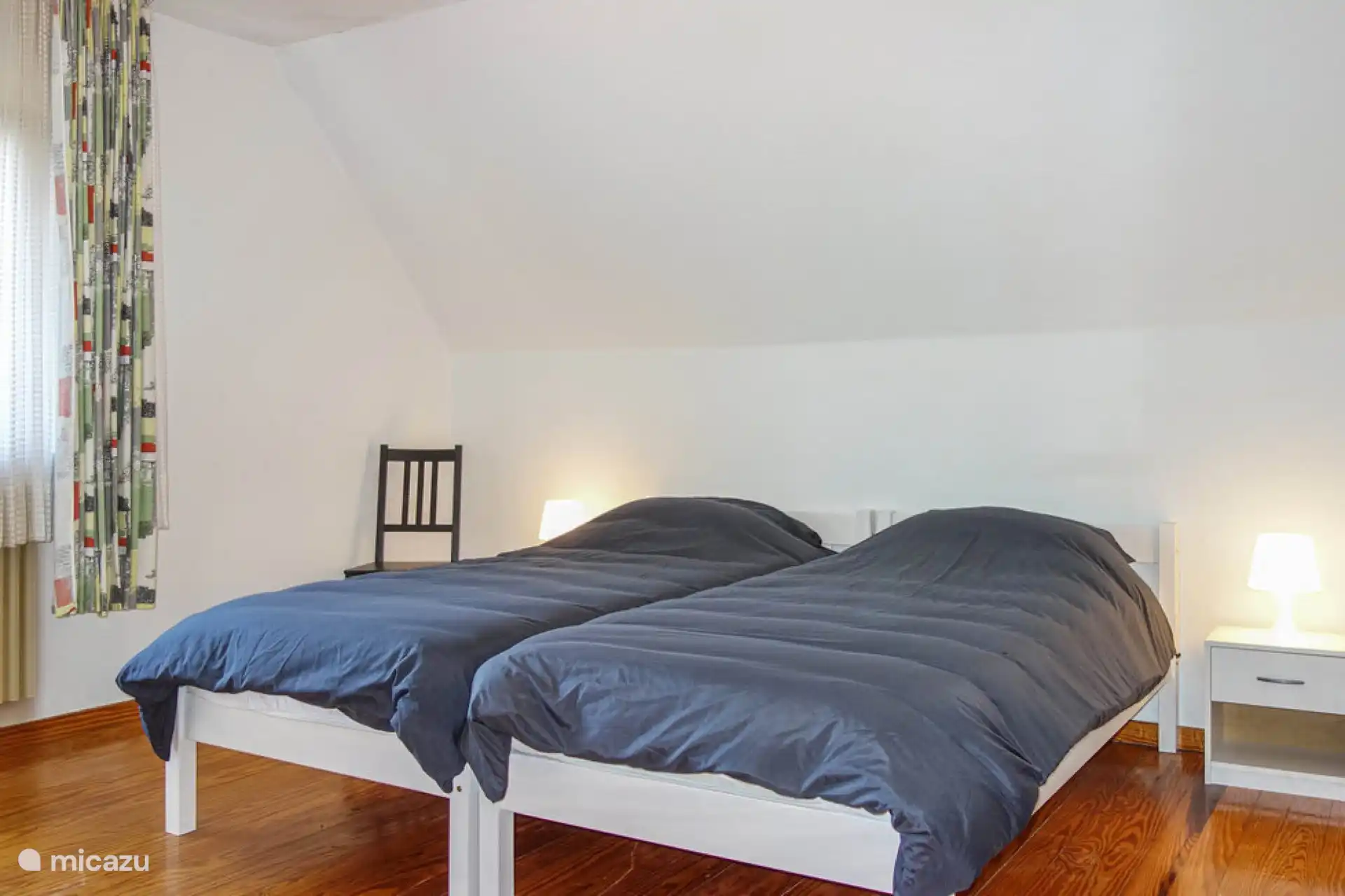 Schlafzimmer im ersten Stock. Zwei Einzelbetten mit Nachttischen für Erwachsene. Ebenfalls vorhanden: ein Kleiderschrank für Kleidung oder andere Gegenstände, ein Spiegel und ein Stuhl.