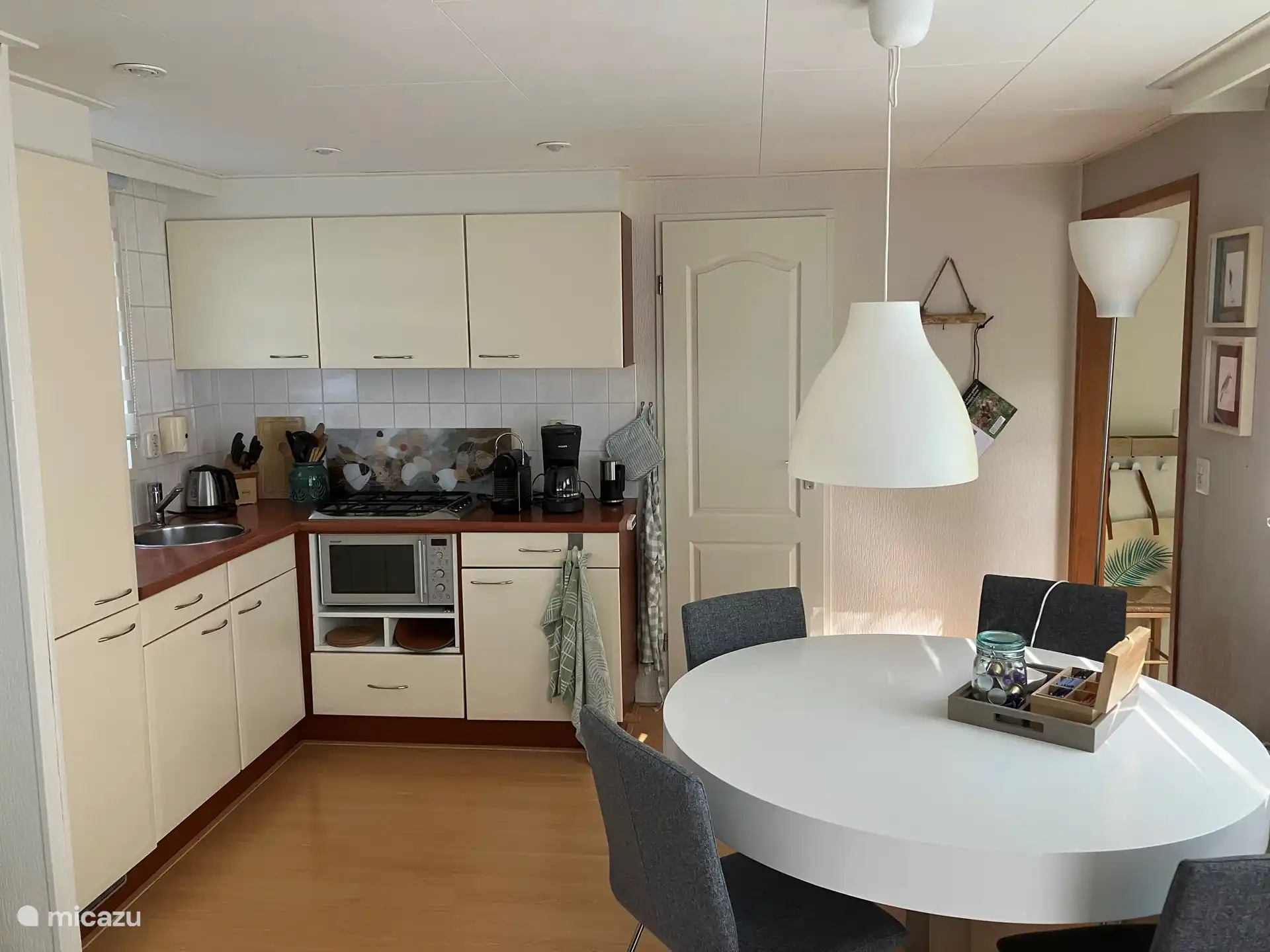 The open kitchen with the round dining table in front of it. There are 4 comfortable chairs around it.