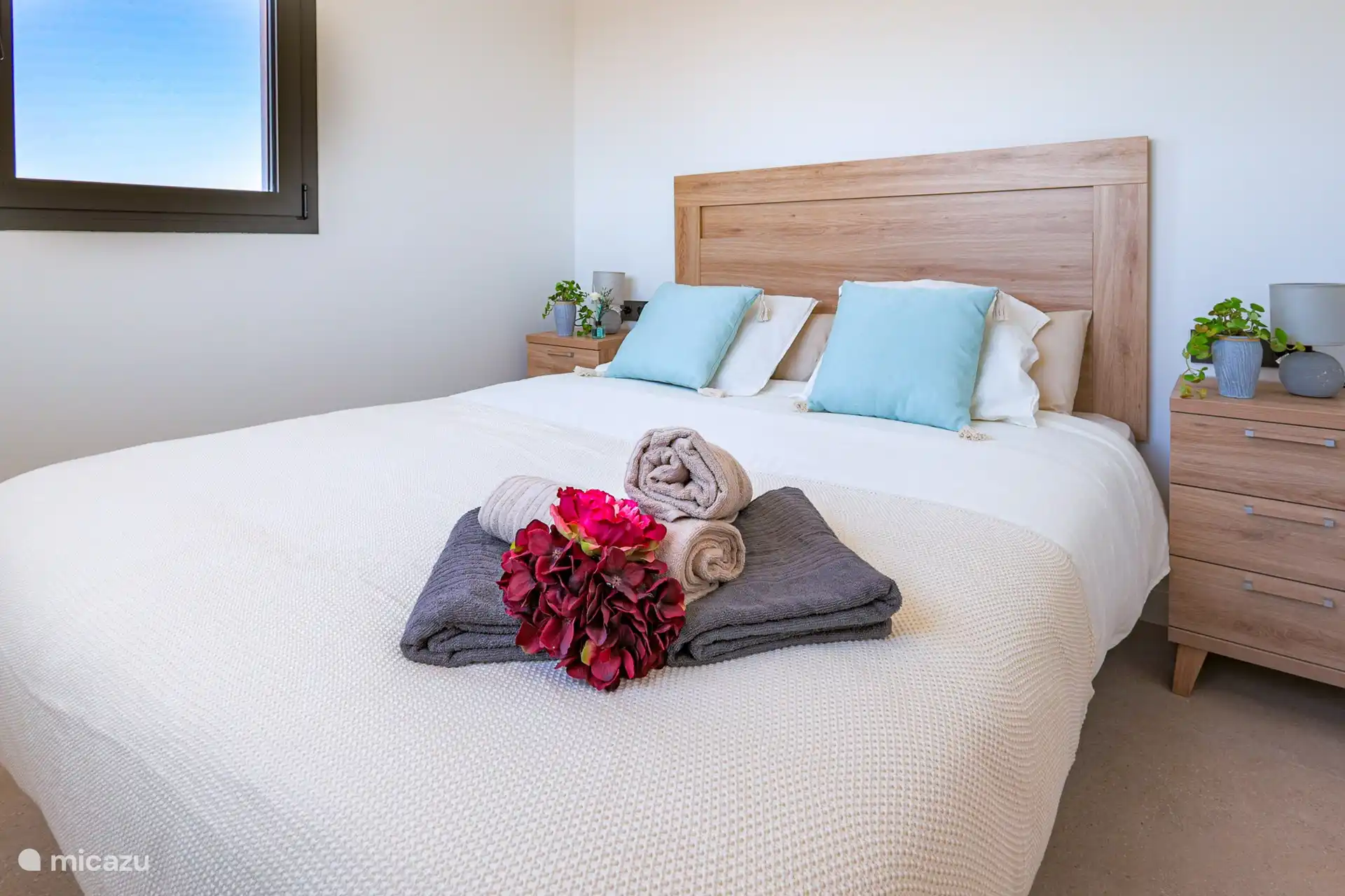 Une chambre moderne avec un lit double spacieux au milieu de la pièce. Le lit est fait avec des draps blancs impeccables et des oreillers moelleux, créant une atmosphère accueillante et sereine. Il y a des tables de chevet des deux côtés du lit.