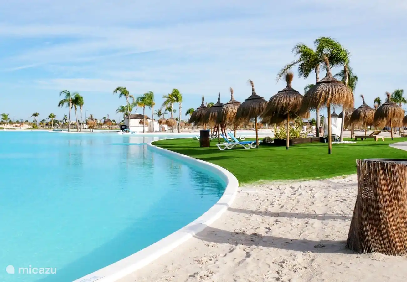 Une image du bord du lac montre une vue imprenable avec une combinaison de sable blanc et doux et d’herbe verte vibrante. Le sable est clair et accueillant, parfait pour se détendre et profiter du soleil. L’herbe qui se connecte au sable est luxuriante et bien entretenue.
