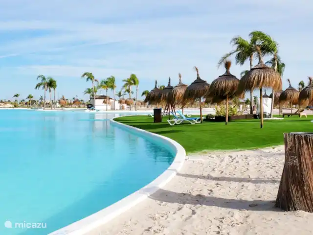Casa SK Santa Rosalia | Espagne, Costa Cálida, Torre Pacheco - appartement Une image du bord du lac montre une vue imprenable avec une combinaison de sable blanc et doux et d’herbe verte vibrante. Le sable est clair et accueillant, parfait pour se détendre et profiter du soleil. L’herbe qui se connecte au sable est luxuriante et bien entretenue.