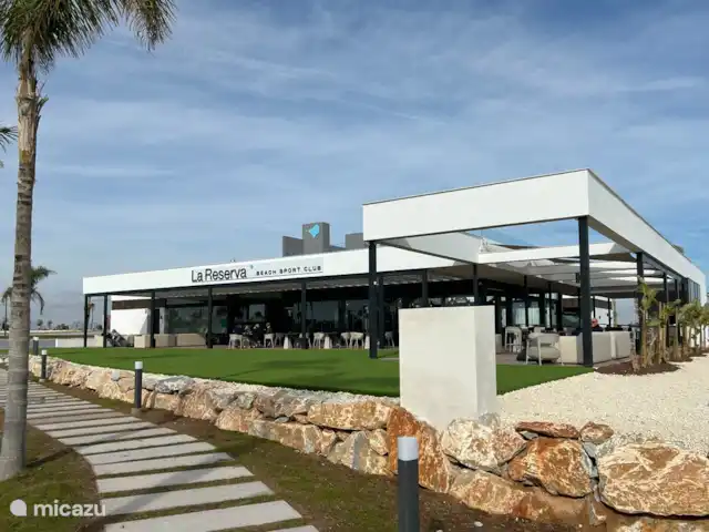 Casa SK Santa Rosalia | Espagne, Costa Cálida, Torre Pacheco - appartement Une photo du Beach Resort Club montre un espace de restauration animé et accueillant au bord de la plage. L’espace est meublé avec des tables en bois élégantes et des chaises confortables, parfaites pour les clients qui souhaitent profiter d’un déjeuner ou d’un dîner tranquille.