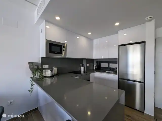 Luxe appartement met zwembadzicht huren in Spanje, Costa Blanca, Alicante - appartement De open keuken met schiereiland vormt het hart van de woning. Het schiereiland biedt niet alleen extra werkruimte, maar creëert ook een gezellige plek om samen te komen tijdens het koken. De keuken is modern ingericht en volledig uitgerust met alle benodigde apparatuur.