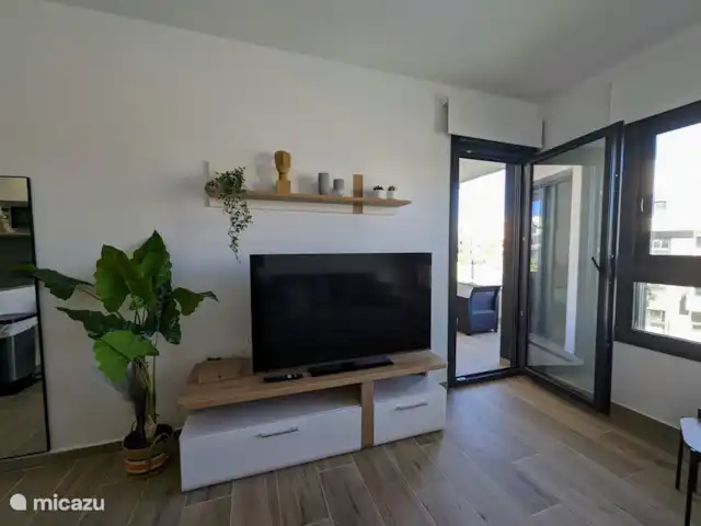 Luxe appartement met zwembadzicht huren in Spanje, Costa Blanca, Alicante - appartement De knusse woonkamer straalt warmte en gezelligheid uit, met comfortabele meubels en een sfeervolle inrichting. Door de grote ramen heb je een prachtig uitzicht op het zwembad, wat een heerlijk gevoel van ruimte en rust geeft.