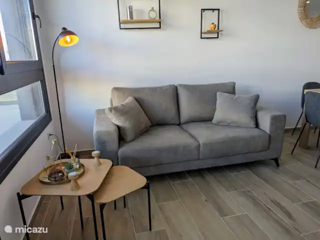 Luxe appartement met zwembadzicht huren in Spanje, Costa Blanca, Alicante - appartement De knusse woonkamer straalt warmte en gezelligheid uit, met comfortabele meubels en een sfeervolle inrichting. Door de grote ramen heb je een prachtig uitzicht op het zwembad, wat een heerlijk gevoel van ruimte en rust geeft.