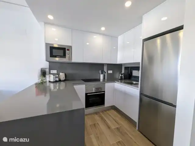 Luxe appartement met zwembadzicht huren in Spanje, Costa Blanca, Alicante - appartement De open keuken met schiereiland vormt het hart van de woning. Het schiereiland biedt niet alleen extra werkruimte, maar creëert ook een gezellige plek om samen te komen tijdens het koken. De keuken is modern ingericht en volledig uitgerust met alle benodigde apparatuur.