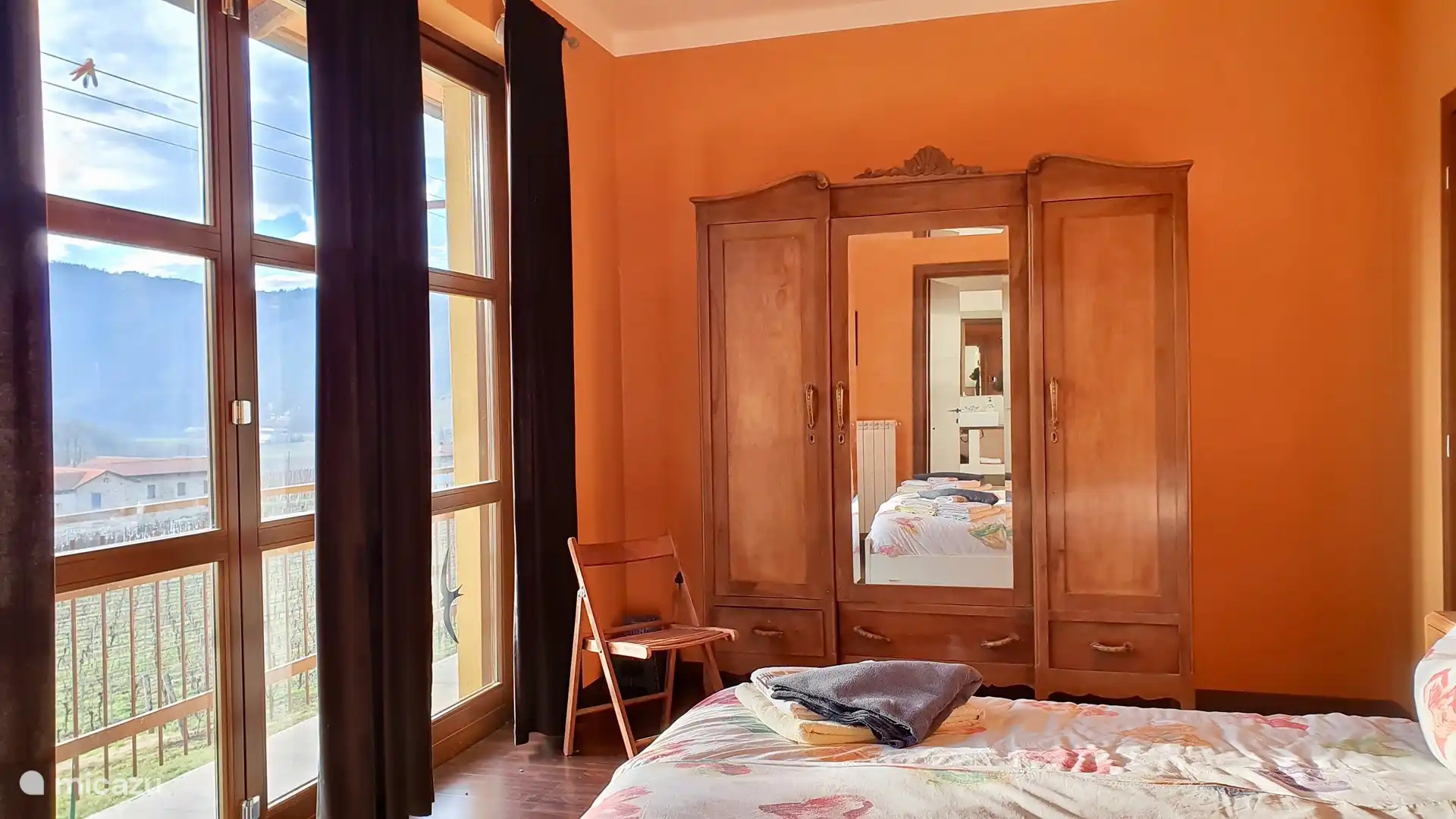 Uno de los dormitorios principales. Esta habitación cuenta con una cama doble y un gran armario de ropa blanca. Acceso directo al balcón, al rellano y al baño con ducha. Vista de los viñedos y a lo lejos la torre medieval de Perletto. 