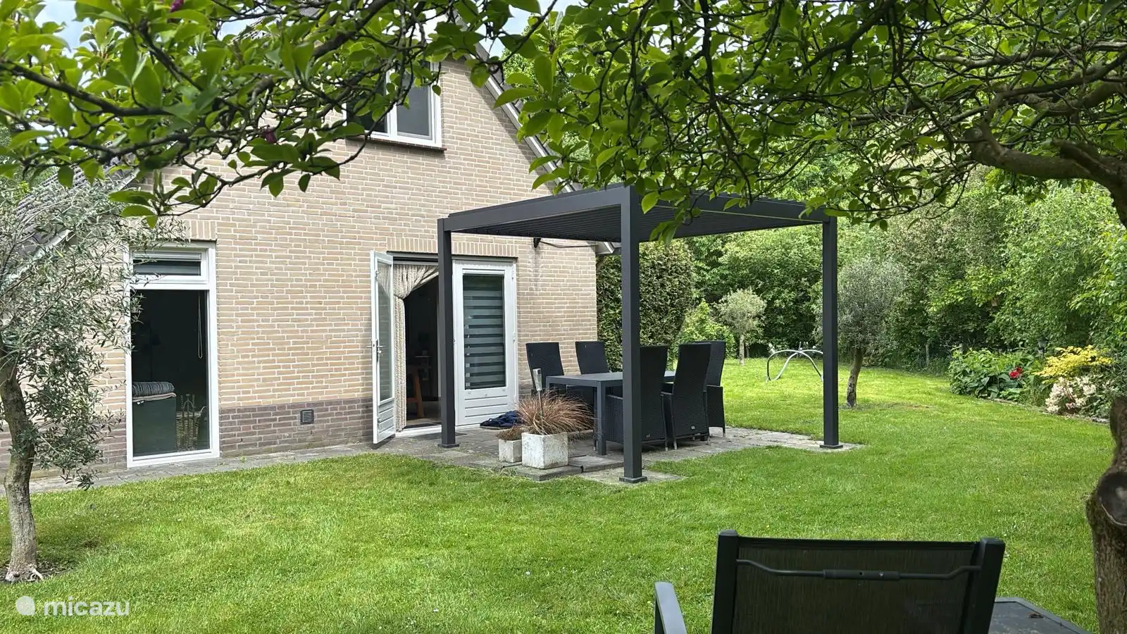 Acogedor jardín trasero verde de 0mheinde, privacidad con pérgola de listones y asientos cómodos.