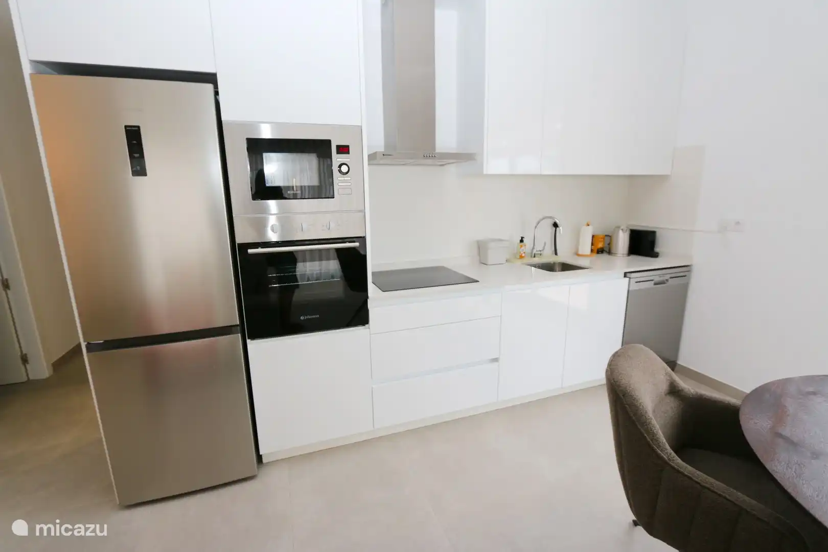 Die offene Küche mit Kühlschrank mit Gefrierfach, Induktionskochfeld, Geschirrspüler und kleinen Küchengeräten.