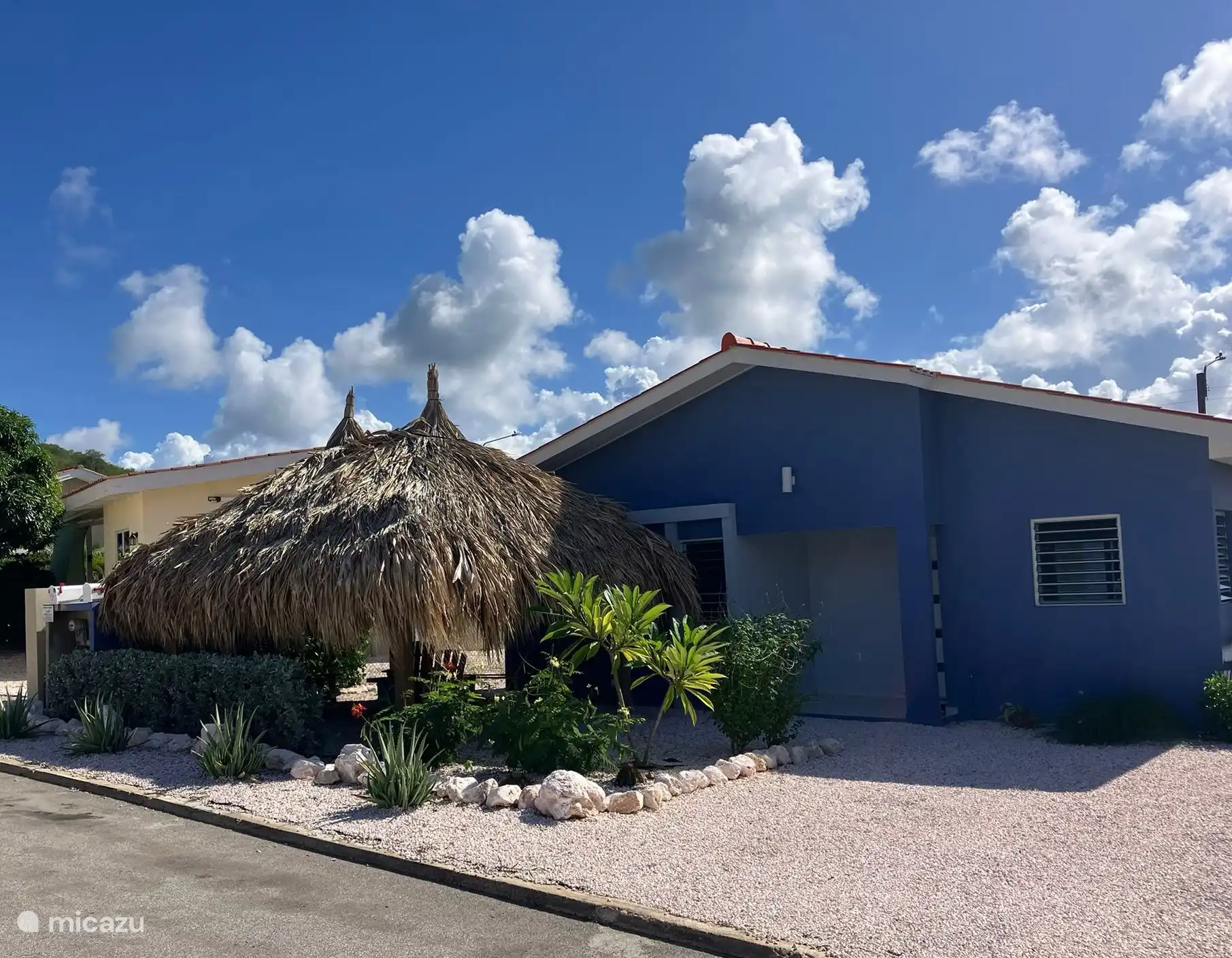 Vooraanzicht van de villa met privé oprit en een comfortabele loungeset onder de palapa – een heerlijke plek om te ontspannen in de avondzon of het Caribische briesje.