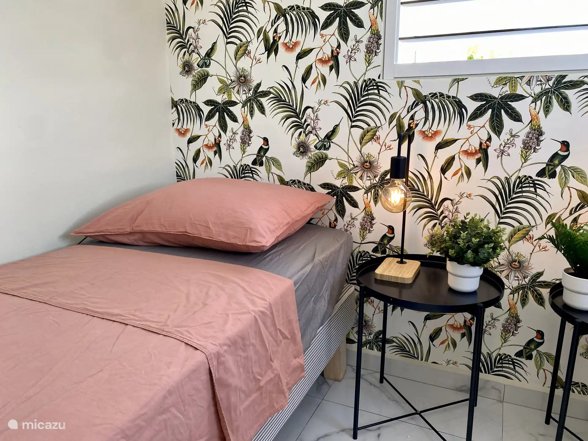 Détail atmosphérique du lit avec papier peint tropical et linge de lit frais - un mélange apaisant de confort et de style caribéen