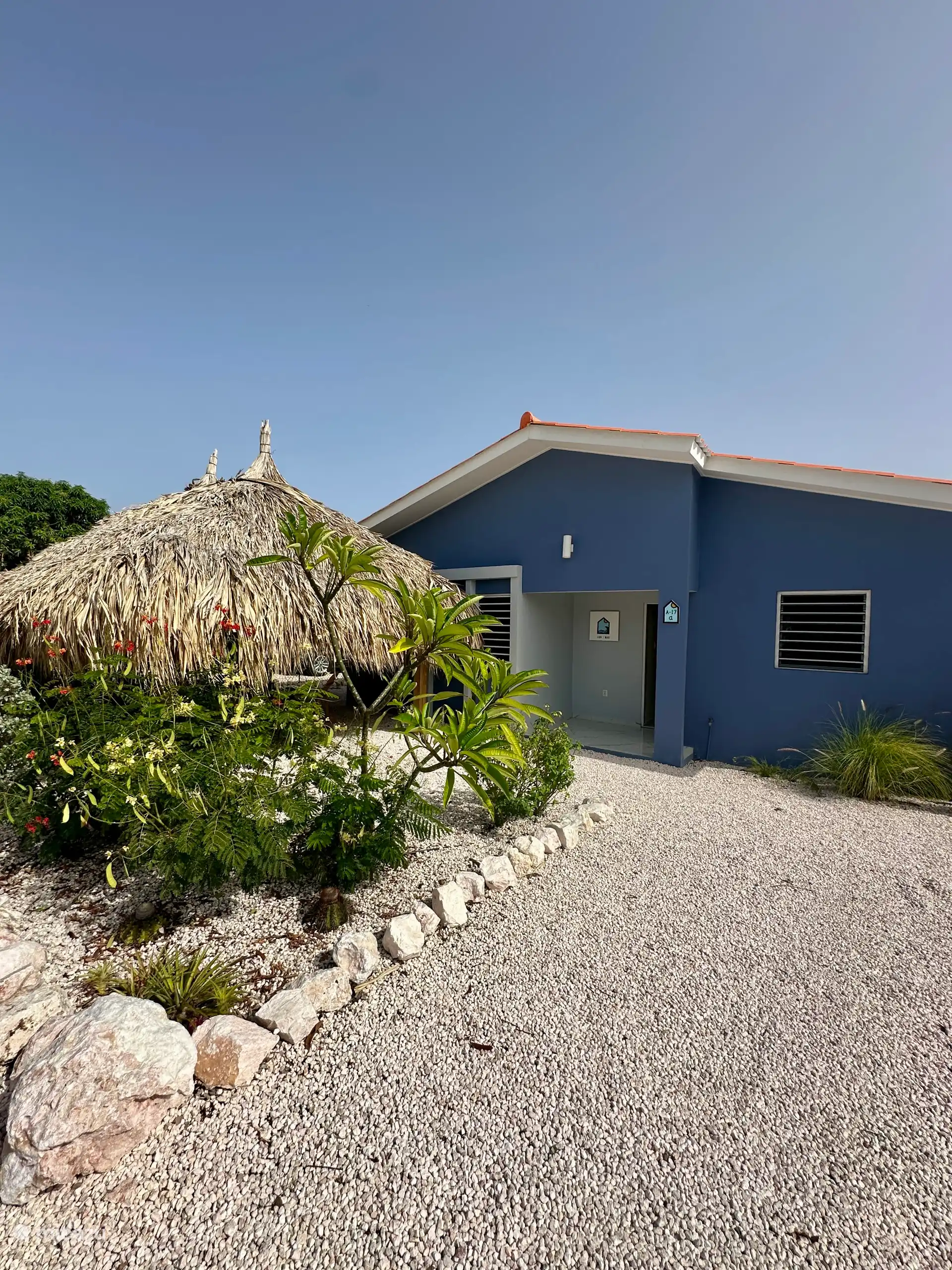 Vooraanzicht van de villa met privé oprit en een comfortabele loungeset onder de palapa – een heerlijke plek om te ontspannen in de avondzon of het Caribische briesje.