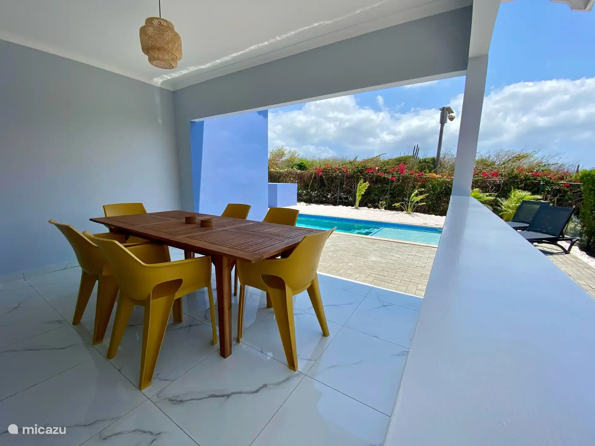 Table à manger avec des chaises confortables sur la véranda semi-ouverte - profitez des repas à l’ombre avec vue sur la piscine privée et le jardin tropical.