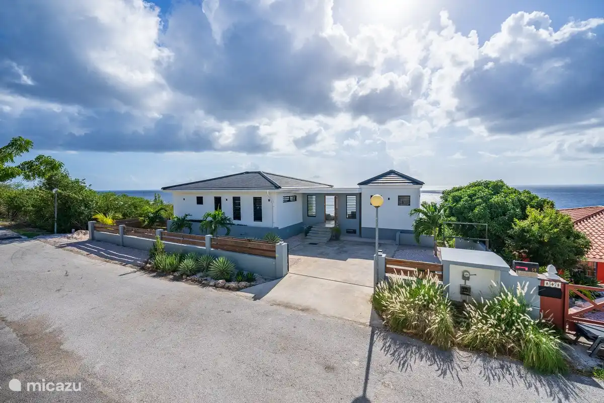 Villa mit Frontansicht mit ausreichend Parkplätzen auf privatem Grundstück und auf der rechten Seite Waschbecken und Kleiderständer für Taucher