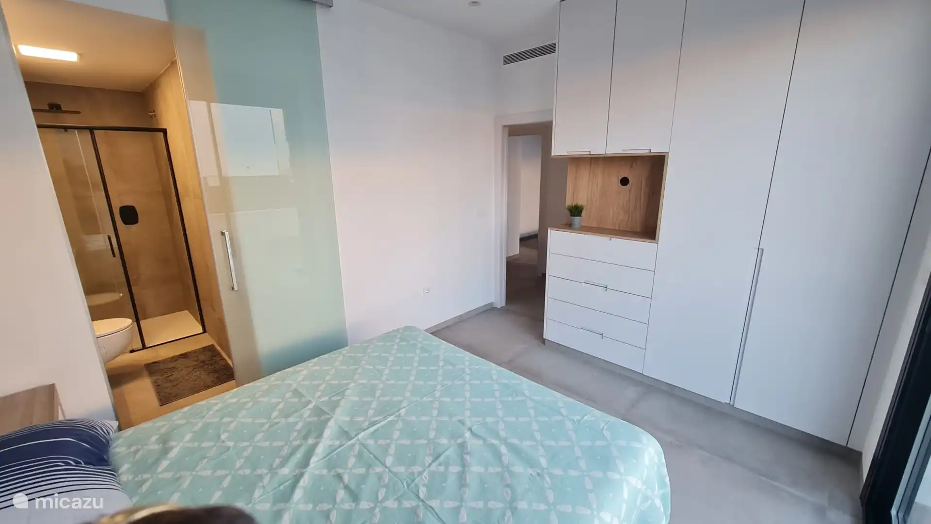 Chambre principale avec armoire encastrée et porte coulissante en verre vers la salle de bain attenante. 