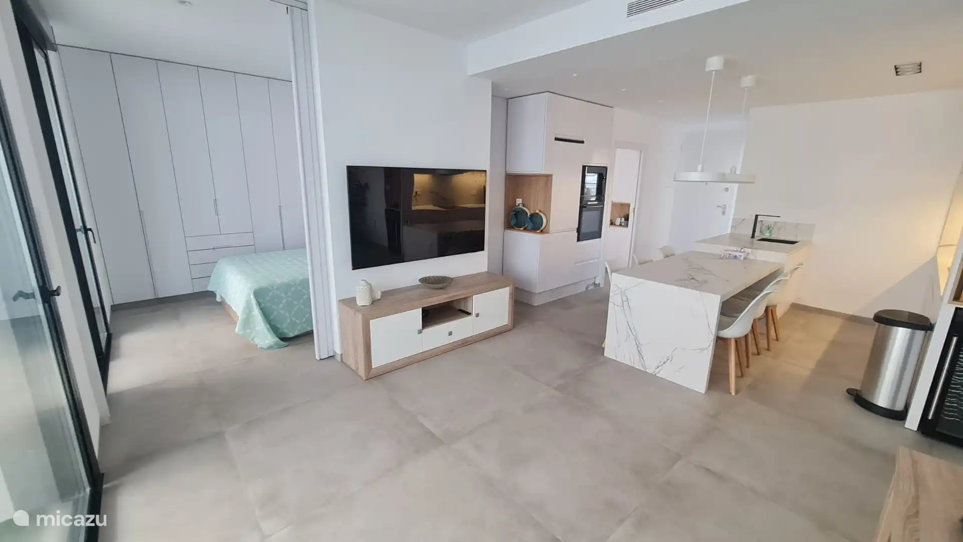 Salon avec grande télévision. À gauche se trouve la 3ème chambre (avec porte coulissante) et à droite de la télévision la 2ème salle de bain. 