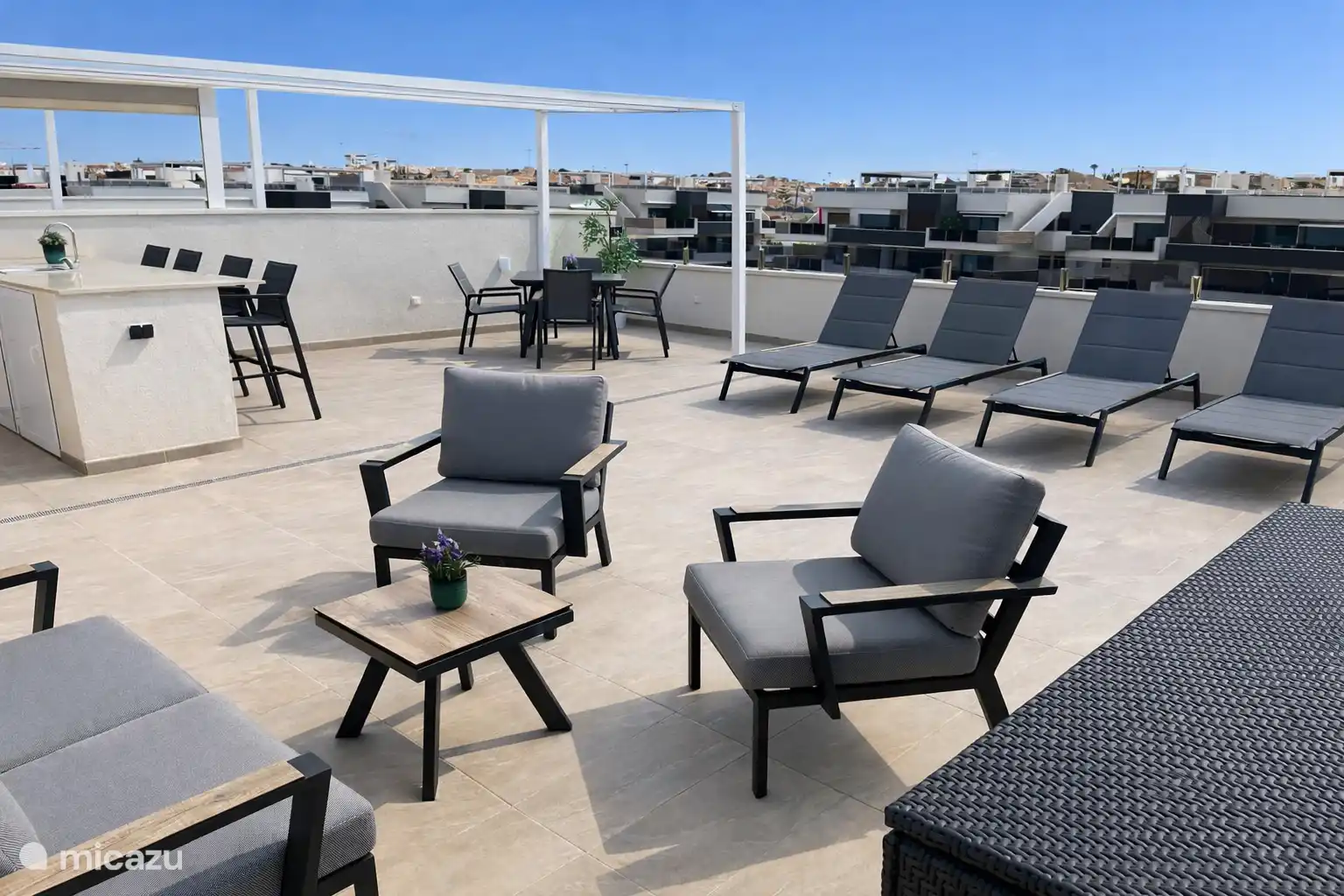 Terraza en la azotea con cocina exterior, mesa de comedor, sala de estar, tumbones y caja de almacenamiento para cojines