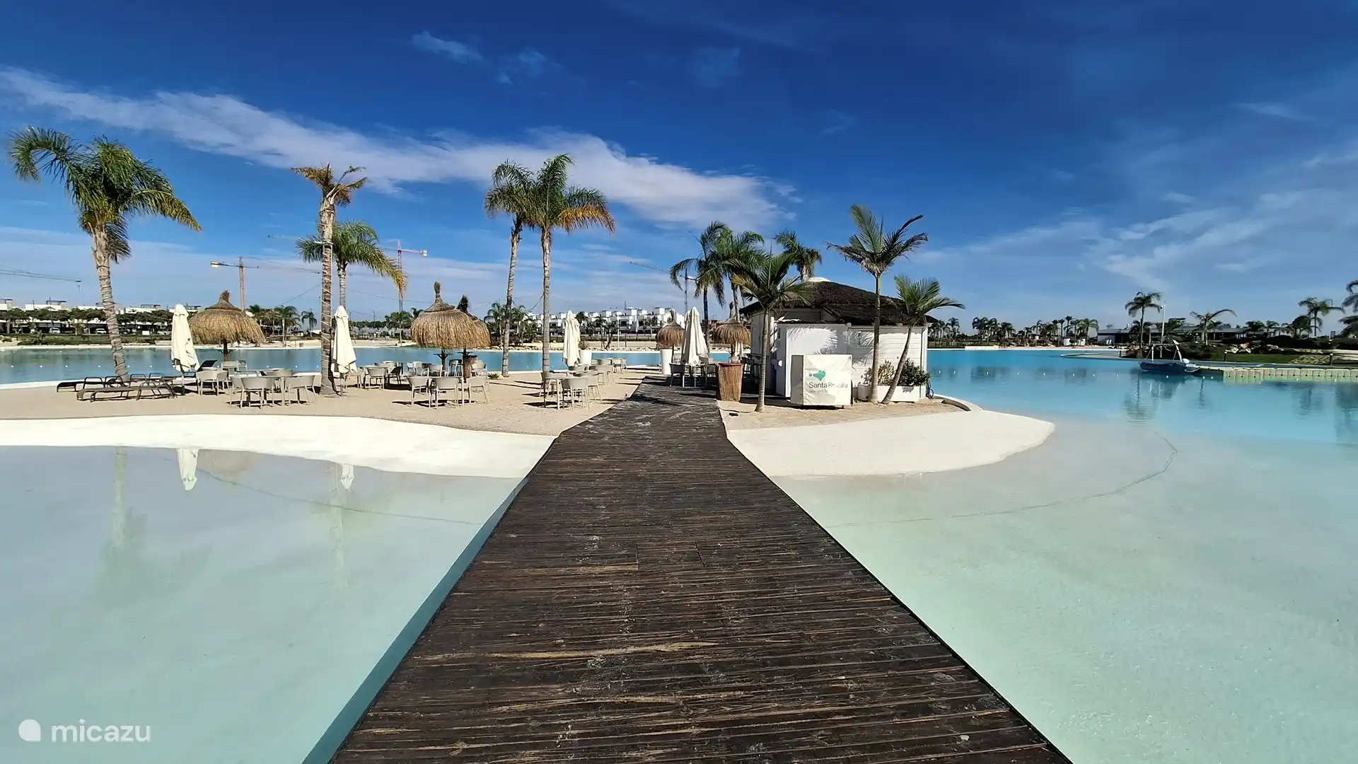 Isla en el lago Santa Rosalía con un bar para bebidas refrescantes, una playa de arena con sombrillas y tumbonas, rodeada de agua azul clara.