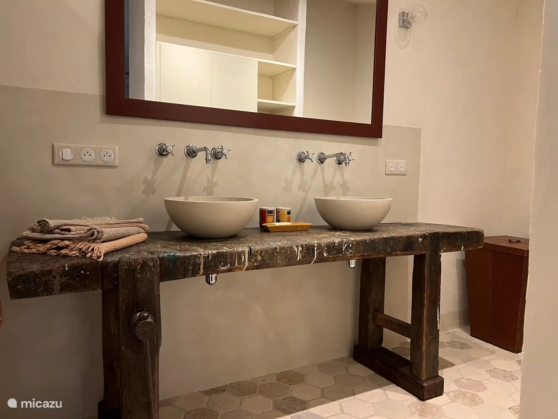 De badkamer aan Kamer 1 heeft 2 wastafels op een antieke schrijnwerkerstafel, een hangtoilet en een ruime douche in béton ciré. 