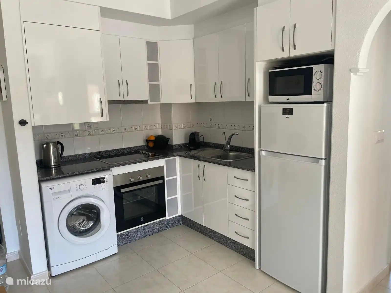 Küche mit Nespresso-Maschine, Waschmaschine, Kühlschrank mit Gefrierfach, Backofen und Mikrowelle.