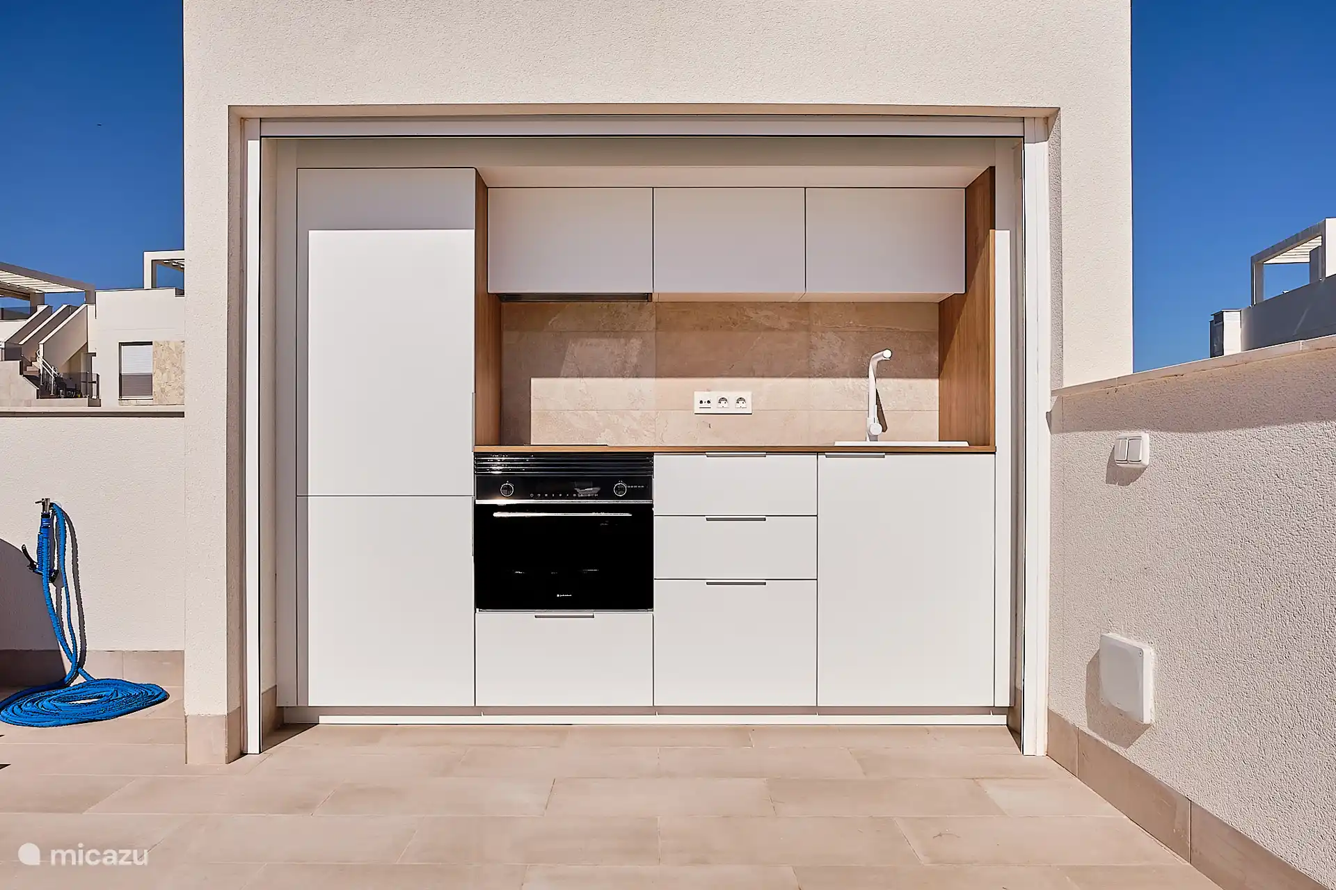 Die Außenküche befindet sich hinter einem Rolltor und hat Zugang zu einem Backofen, einem Herd, einer Dunstabzugshaube, einem Kühlschrank, einem Gefrierschrank und einer Spüle.